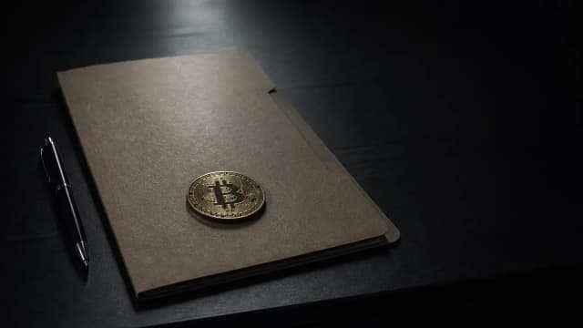 Geschlossene Aktenmappe, Stift und Bitcoin-Münze auf einem dunklen Schreibtisch – Sinnbild für eine Anzeige, wenn Krypto gestohlen wurde